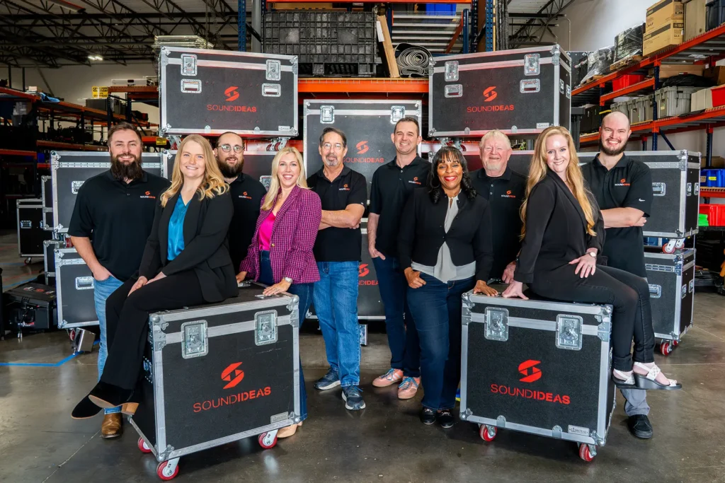 Corporate leadership team posing in warehouse with branded equipment cases, representing teamwork, trust, and organizational alignment