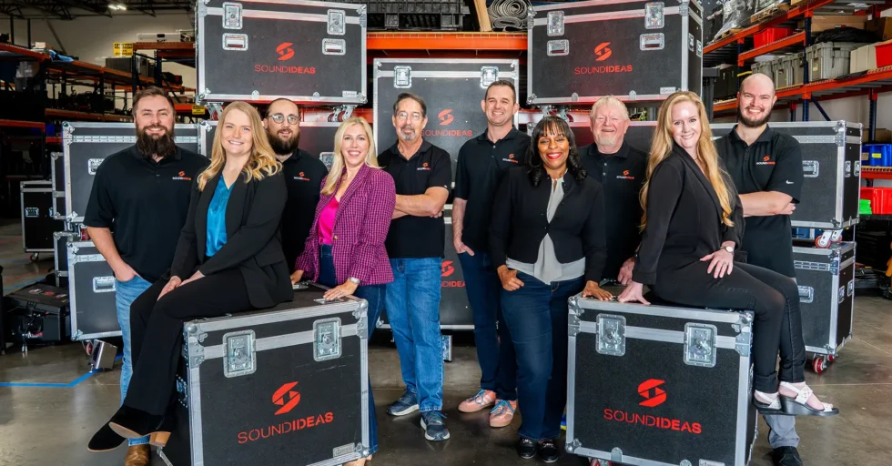 Corporate leadership team posing in warehouse with branded equipment cases, representing teamwork, trust, and organizational alignment